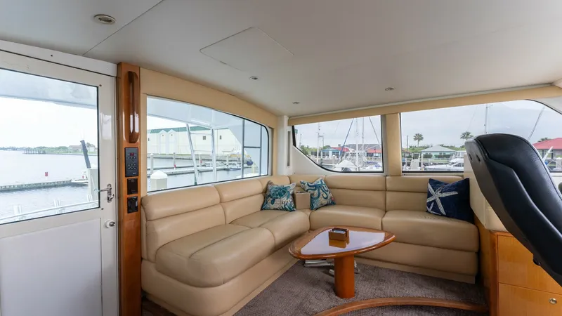 Slide: The Image of Enclosed Bridge Lounge Area This inviting enclosed bridge lounge on the 2001 Viking 65 features plush cream leather seating arranged in an L-shape, offering comfort and style. The large windows provide panoramic views of the marina, enhancing the sense of space and light. A wooden c - 6767188