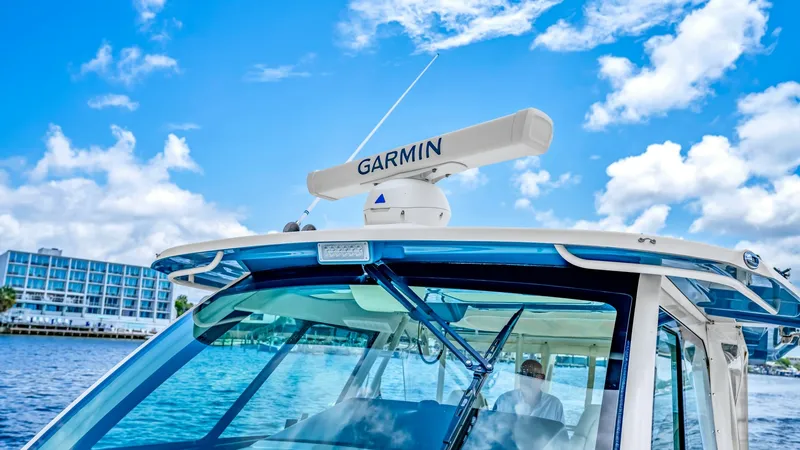 Slide: The Image of Helm Station with Garmin Radar This image showcases the helm station of the Grady-White Canyon 456, featuring a sleek, modern design with an integrated Garmin radar system. The expansive windshield offers unobstructed visibility, enhanced by the clear blue sky and waterscape in the bac - 6725181