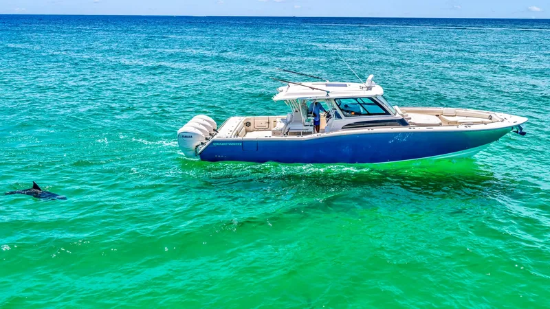 Slide: The Image of Side Profile on Open Water The Grady-White Canyon 456 cuts gracefully through vibrant turquoise waters, showcasing its sleek design and robust build. The spacious deck and multiple outboard engines underscore its power and capability for offshore adventures. The elegant lines and m - 6725199