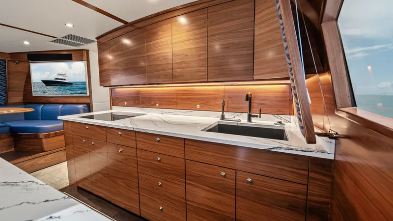Slide: The Image of Galley with Modern Wood Finish The galley of the 2024 Viking 64 Convertible 'Southern Grace' boasts sleek, contemporary wood cabinetry perfectly complemented by elegant marble countertops. This space offers ample storage and workspace, highlighted by under-cabinet lighting that enhance - 7541836