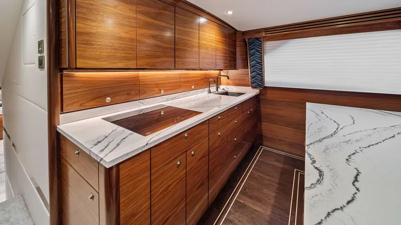 Slide: The Image of Sleek Galley with Marble Accents This luxurious galley on the Viking 64 Convertible features beautifully crafted wood cabinetry and elegant marble countertops. The integrated cooktop and stainless steel sink offer both functionality and style, while the under-cabinet lighting ensures a w - 7541820