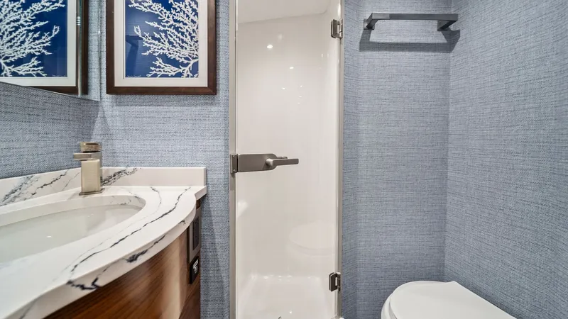Slide: The Image of VIP Bathroom This luxurious bathroom on the 2024 Viking 64 Convertible features a sleek, modern design with a glass-enclosed shower and a stylish vanity. The space is adorned with nautical-themed artwork and premium fixtures, providing a touch of elegance. Soft lighti - 7541851