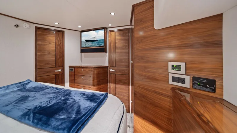 Slide: The Image of Luxurious Master Stateroom The master stateroom aboard the 2024 Viking 64 Convertible exudes elegance with its rich wood finishes and plush bedding. A large flat-screen TV is mounted for entertainment, complemented by sophisticated ambient lighting. Ample storage and modern control - 7541843