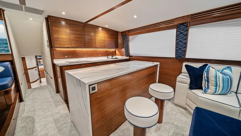 Slide: The Image of Galley and Salon Seating Area The galley of the 2024 Viking 64 Convertible is elegantly designed with rich wooden cabinetry and a sleek marble countertop, offering both functionality and style. Adjacent to the galley, a comfortable salon seating area features plush sofas with nautical - 7541819