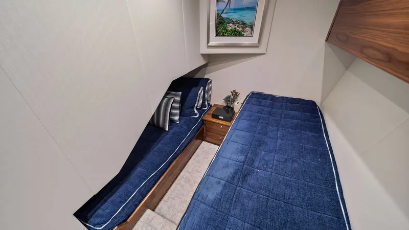 Slide: The Image of Guest Cabin with Twin Berths This inviting guest cabin on the 2024 Viking 64 Convertible features comfortable twin berths with plush blue bedding, creating a cozy retreat for guests. The space is enhanced by elegant wood accents and soft lighting, providing a warm and welcoming ambia - 7541855