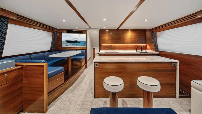 Slide: The Image of Spacious Interior Salon with Galley The salon of the 2024 Viking 64 Convertible 'Southern Grace' features an elegant open-plan layout with a luxurious galley. Rich wood finishes and sleek lines define the space, complemented by plush blue seating and a stylish dining nook. Recessed lighting - 7541818