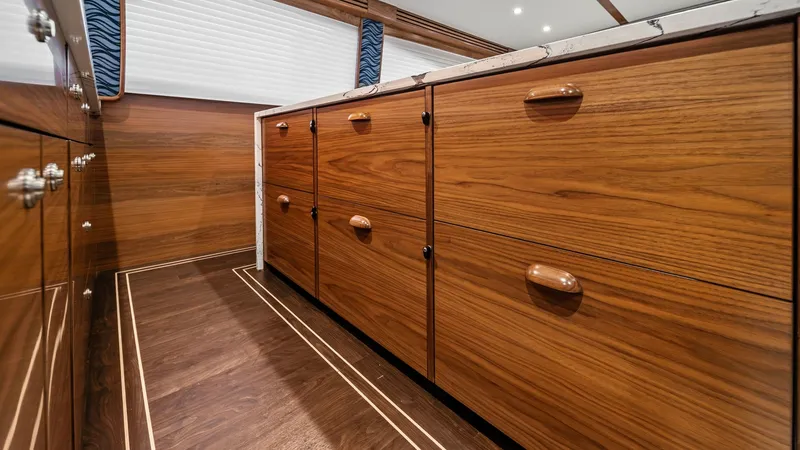 Slide: The Image of Galley Storage Cabinets The galley of the 2024 Viking 64 Convertible showcases elegant wooden cabinetry, offering ample storage space for all culinary essentials. The warm wood tones and polished finishes complement the yacht's sophisticated interior design. Recessed lighting en - 7541822