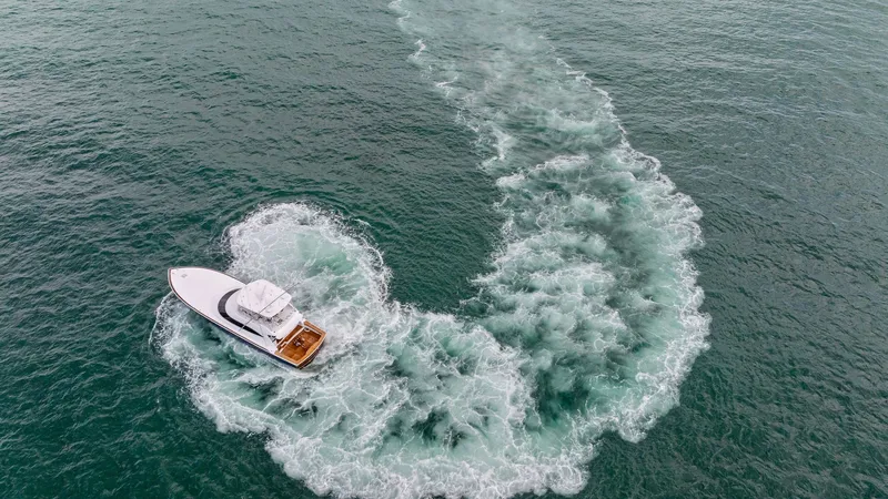 Slide: The Image of Aerial View of Yacht in Motion This dynamic aerial shot captures the 2024 Viking 64 Convertible 'Southern Grace' carving gracefully through the water. The vessel's sleek design is highlighted by its powerful wake, showcasing its exceptional performance and agility. The spacious aft dec - 7541896