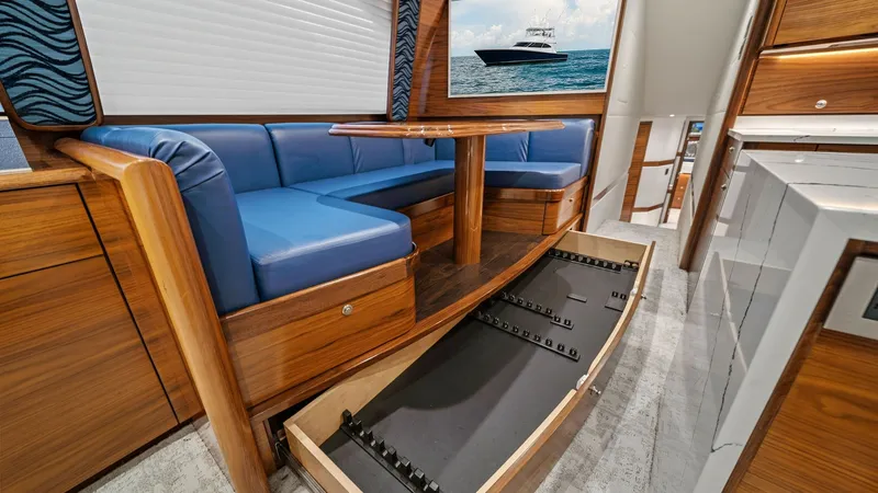 Slide: The Image of Salon with Convertible Seating Area The salon of the 2024 Viking 64 Convertible showcases a luxurious seating area with elegant wood finishes and plush blue upholstery. The convertible table and seating offer flexibility, while the storage drawer beneath provides ample space for essentials. - 7541824