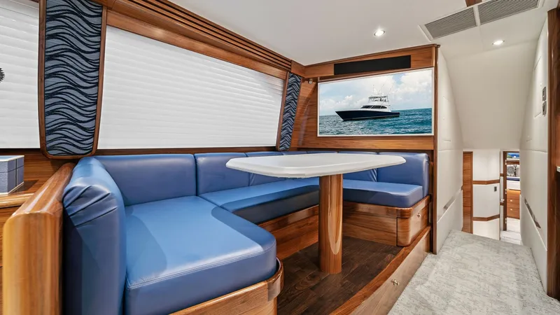 Slide: The Image of Elegant Dinette with Ocean Views This beautifully crafted dinette area on the 2024 Viking 64 Convertible features plush blue seating and a polished wooden table, offering a comfortable space for dining or relaxation. The surrounding windows provide ample natural light and stunning ocean - 7541816
