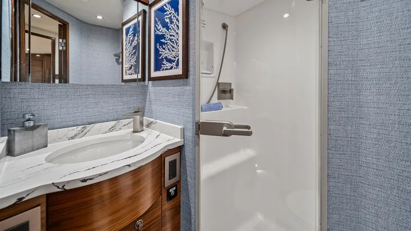 Slide: The Image of VIP Bathroom This elegant ensuite bathroom on the 2024 Viking 64 Convertible features a sleek, marble-topped vanity with a stylish round sink. The space is enhanced by sophisticated wood cabinetry and modern fixtures, complemented by tasteful wall art. The spacious sh - 7541852