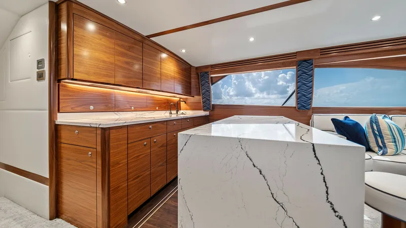 Slide: The Image of Galley with Marble Countertops The galley of the 2024 Viking 64 Convertible 'Southern Grace' features exquisite marble countertops and rich wood cabinetry, offering a luxurious yet functional space. Under-cabinet lighting enhances the warm wood tones and illuminates the work area, whil - 7541837
