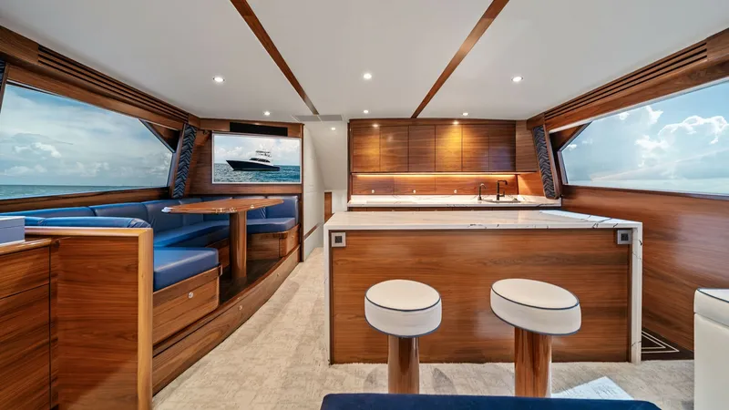Slide: The Image of Spacious Galley and Salon Area This image showcases the luxurious galley and salon of the 2024 Viking 64 Convertible, Southern Grace. The space features rich wood finishes and plush blue seating, creating an inviting atmosphere. Large windows offer panoramic ocean views, while modern l - 7541833