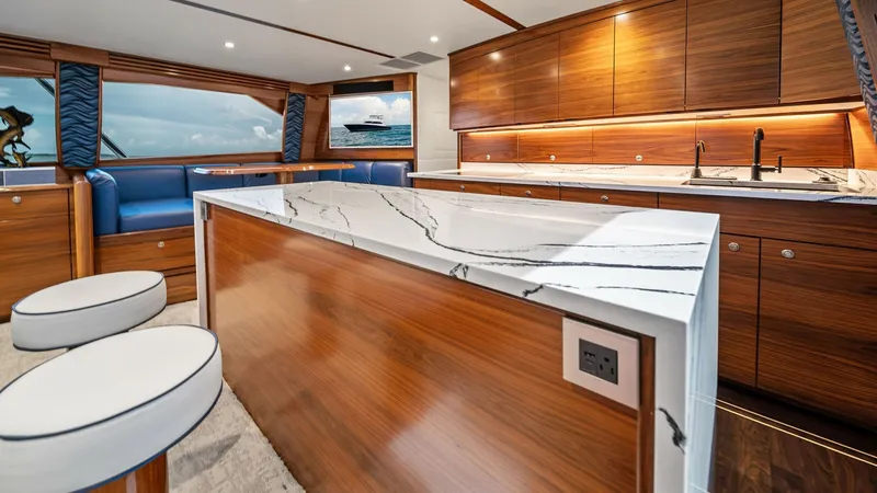Slide: The Image of Luxury Galley with Marble Island The galley of the 2024 Viking 64 Convertible, Southern Grace, is elegantly designed with rich wood cabinetry and a striking marble island. The spacious layout features modern appliances, under-cabinet lighting, and a seamless integration with the salon ar - 7541835