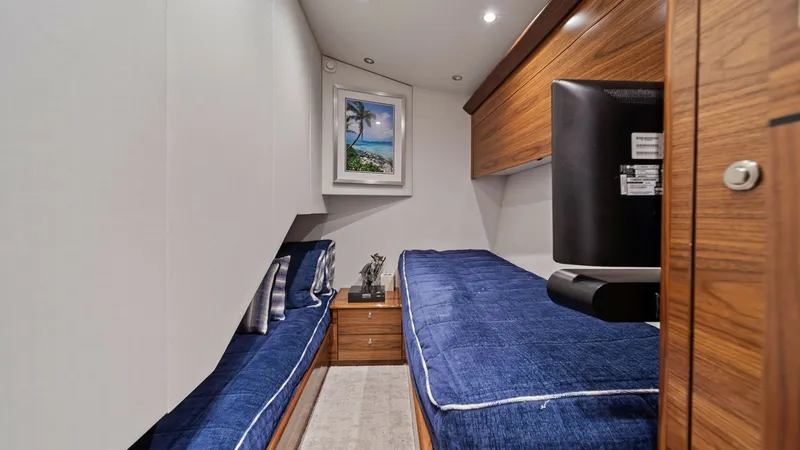 Slide: The Image of Guest Stateroom with Twin Berths This cozy guest stateroom on the 2024 Viking 64 Convertible features twin berths, offering comfort and style with blue upholstered bedding. Rich wood finishes provide a warm ambiance, complemented by modern overhead lighting. A flat screen TV and a scenic - 7541853