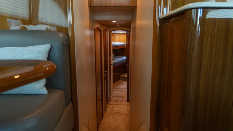 Slide: The Image of 2009 Viking 50 Convertible "Jammin" - Passageway Leading to Staterooms This passageway on the 2009 Viking 50 Convertible 'Jammin' leads to the staterooms, showcasing elegant wood paneling and soft carpeting. The warm lighting enhances the inviting atmosphere, while the solid wood doors provide access to the comfortable sleep - 7018195