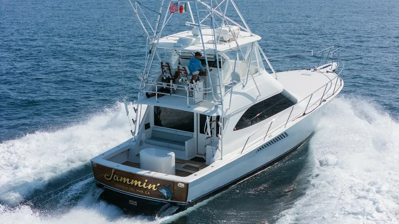 Slide: The Image of 2009 Viking 50 Convertible "Jammin" - Aft-starboard view highlighting the yacht's graceful profile and on-water presence. This image showcases the sleek aft deck and flybridge of the 2009 Viking 50 Convertible, 'Jammin'. The spacious aft deck is designed for both relaxation and sport fishing, featuring ample seating and a sturdy fighting chair. Above, the flybridge offers an - 7018226