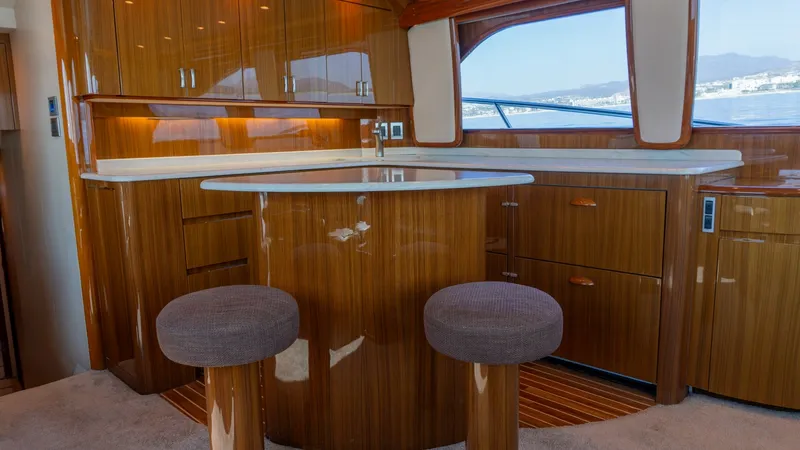 Slide: The Image of 2009 Viking 50 Convertible "Jammin" - Galley with Breakfast Bar The galley on the 2009 Viking 50 Convertible 'Jammin' features high-gloss wooden cabinetry and a sleek, integrated breakfast bar with upholstered stools. Expansive windows provide panoramic views, enhancing the open and airy atmosphere. The polished count - 7018171