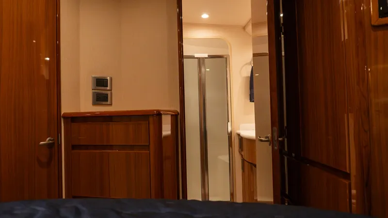 Slide: The Image of 2009 Viking 50 Convertible "Jammin" - Master Stateroom Ensuite Entrance The image showcases the entrance to the master stateroom and its adjoining ensuite bathroom on the 2009 Viking 50 Convertible. Rich wood finishes and ambient lighting create a warm and inviting atmosphere. The ensuite features a modern, sleek shower and e - 7018203