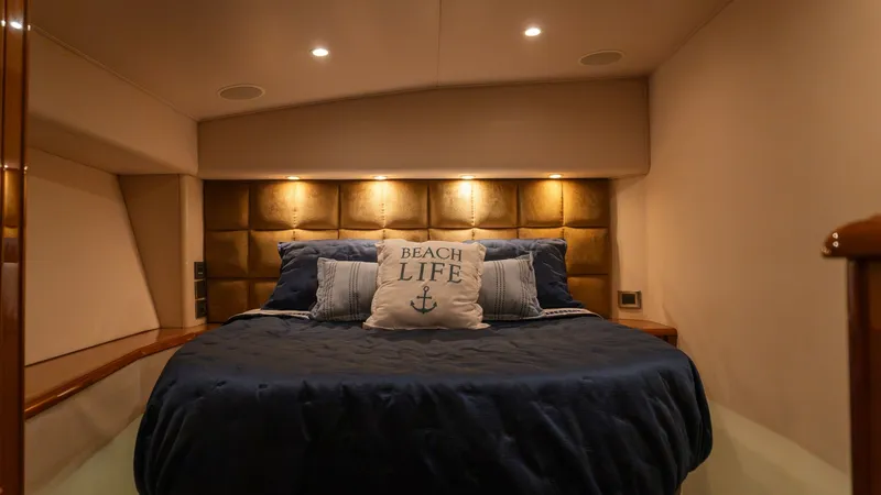 Slide: The Image of 2009 Viking 50 Convertible "Jammin" - Luxurious Forward Stateroom This inviting forward stateroom on the Viking 50 Convertible features a plush, queen-sized bed with elegant navy bedding and decorative cushions. The warm, ambient lighting highlights the rich, padded headboard, enhancing the cozy and sophisticated atmosp - 7018200