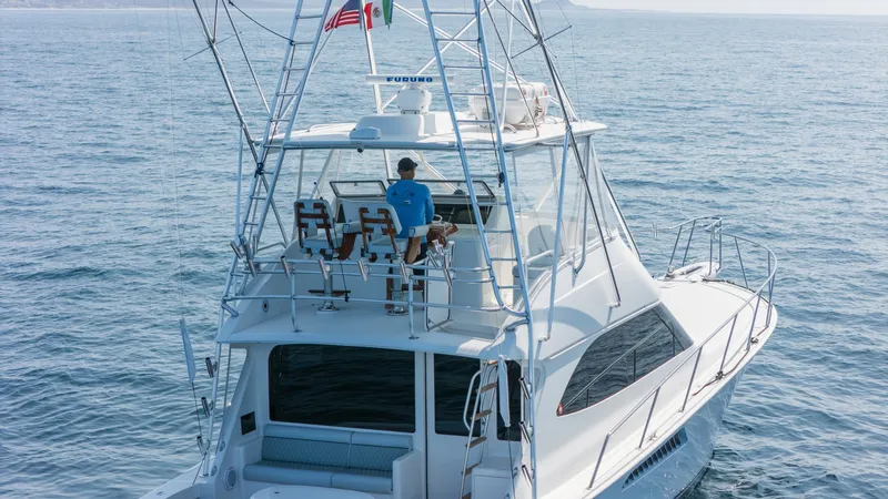 Slide: The Image of 2009 Viking 50 Convertible "Jammin" - Aft View Showcasing the Elevated Flybridge Helm Station and the Yacht's Spacious, Open-Air Design. The flybridge of the 2009 Viking 50 Convertible 'Jammin' offers a commanding view with its elevated helm station. Equipped with dual captain's chairs and a sturdy T-top, this area provides a perfect vantage point for navigation and relaxation. The sleek, - 7018178