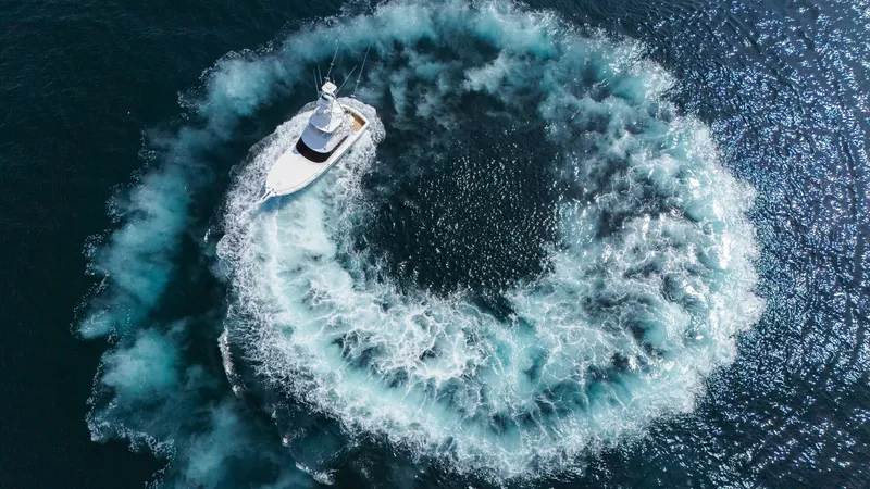 Slide: The Image of 2009 Viking 50 Convertible "Jammin" - Demonstrating Reverse Thrust and Maneuverability. This impressive aerial shot captures the Viking 50 Convertible, 'Jammin', maneuvering with precision, creating a dramatic wake pattern in the deep blue sea. The vessel's sleek lines and powerful performance are highlighted as it carves through the water, - 7018220