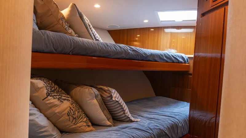 Slide: The Image of 2009 Viking 50 Convertible "Jammin" - Cozy Twin Bunk Cabin Interior This comfortable twin bunk cabin on the 2009 Viking 50 Convertible features rich wood finishes and plush bedding for a relaxing retreat. The overhead lighting creates a warm ambiance, while the cabin's design maximizes space with neatly arranged bunks. A - 7018196