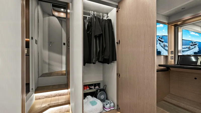 Slide: The Image of Guest Cabin Wardrobe and Entrance This image showcases the guest cabin entrance with a spacious wardrobe on the Absolute 52 Navetta. The wardrobe features ample hanging space and shelves, highlighted by soft, ambient lighting that enhances the sleek wood finish. The elegant hallway leads - 6851820