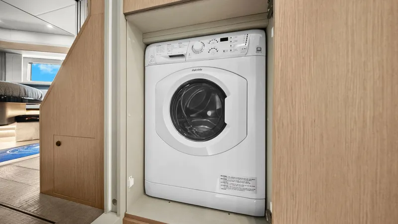 Slide: The Image of Compact Laundry Area This image showcases a neatly integrated laundry space aboard the 2024 Absolute 52 Navetta. The washing machine is smartly concealed within a cabinet, maximizing the use of space without compromising on functionality. The light wood finishes and adjacent - 6851824