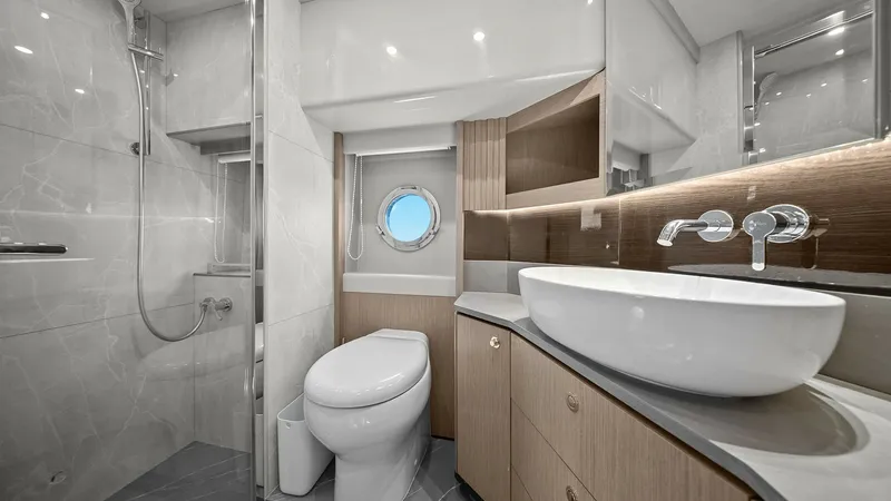 Slide: The Image of Elegant En-Suite Bathroom This stylish en-suite bathroom on the Absolute 52 Navetta features a sleek modern design with high-quality finishes. The space is highlighted by a contemporary vessel sink, elegant wood cabinetry, and a glass-enclosed rainfall shower. A circular porthole - 6851822
