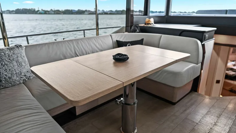 Slide: The Image of Salon Seating with Dining Table The salon of the 2024 Absolute 52 Navetta showcases a stylish and comfortable seating area with a sleek, extendable dining table. Large windows provide ample natural light and panoramic views, enhancing the inviting atmosphere. The modern design and high- - 6851805