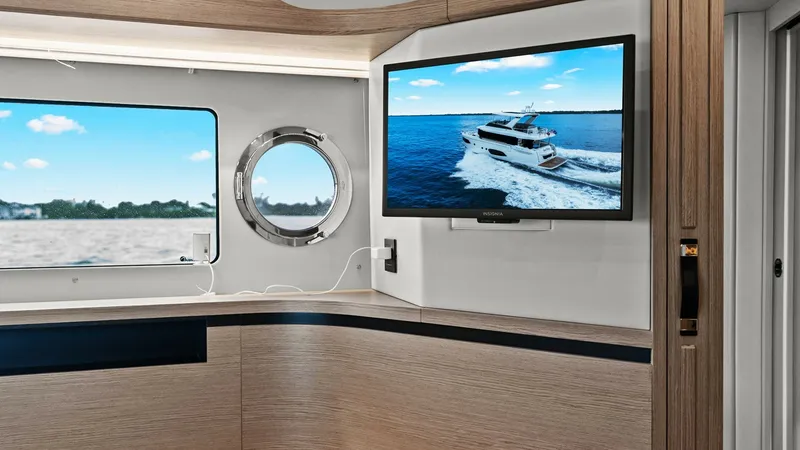 Slide: The Image of Guest Cabin with Port View This guest cabin aboard the 2024 Absolute 52 Navetta features a sleek, modern design with light wood finishes and a large flat-screen TV. The room is enhanced by natural light streaming through the round porthole, offering picturesque ocean views. The cle - 6851818