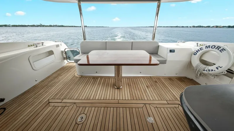 Slide: The Image of Aft Deck with Teak Flooring The aft deck of the Absolute 52 Navetta showcases elegant teak flooring, providing a warm and inviting ambiance. A polished wooden table is centrally positioned, offering a perfect spot for alfresco dining while enjoying expansive water views. The comfort - 6851771