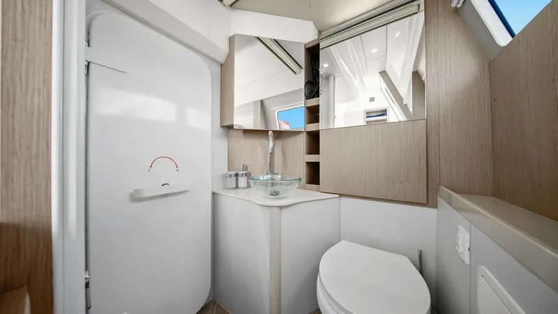 Slide: The Image of Modern Ensuite Bathroom This bright and modern ensuite bathroom on the Absolute 52 Navetta features sleek wood paneling and a contemporary glass sink. The space is thoughtfully designed with ample natural light from the window, enhancing the minimalist aesthetic. Practical stora - 6851837