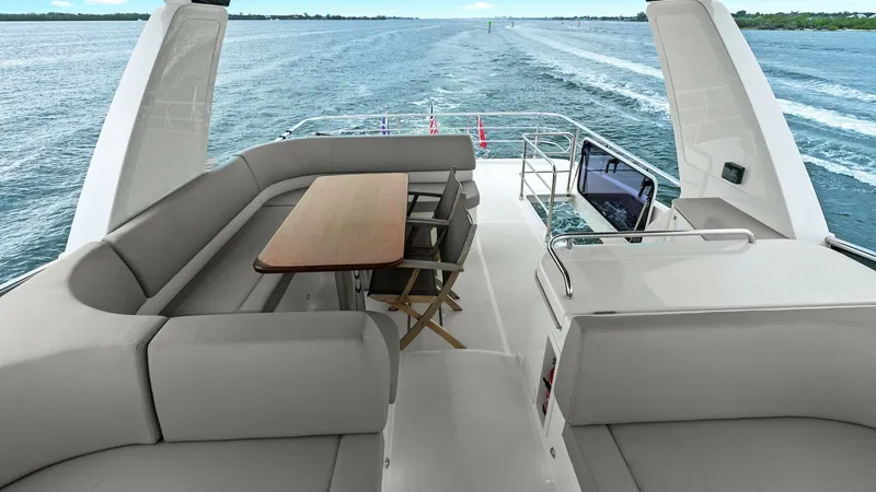 Slide: The Image of Flybridge Lounge and Helm Station The spacious flybridge of the 2024 Absolute 52 Navetta offers a comfortable lounge area with plush seating and a sleek wooden table, perfect for socializing and enjoying panoramic views. Adjacent to the seating, the helm station is equipped with modern na - 6851785