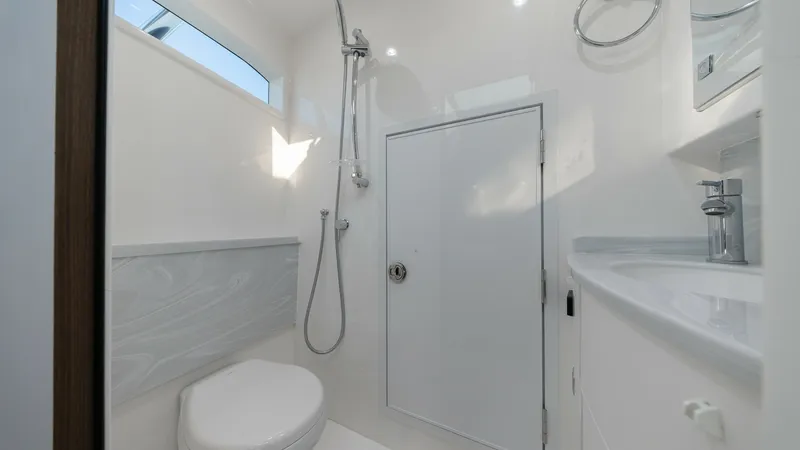 Slide: The Image of Modern Yacht Bathroom This sleek and contemporary bathroom on the 2022 Valhalla Boatworks V-46 features a clean, white design with high-quality fixtures. The space includes a compact shower area, a stylish sink, and a toilet, all illuminated by natural light from the window ab - 7162312