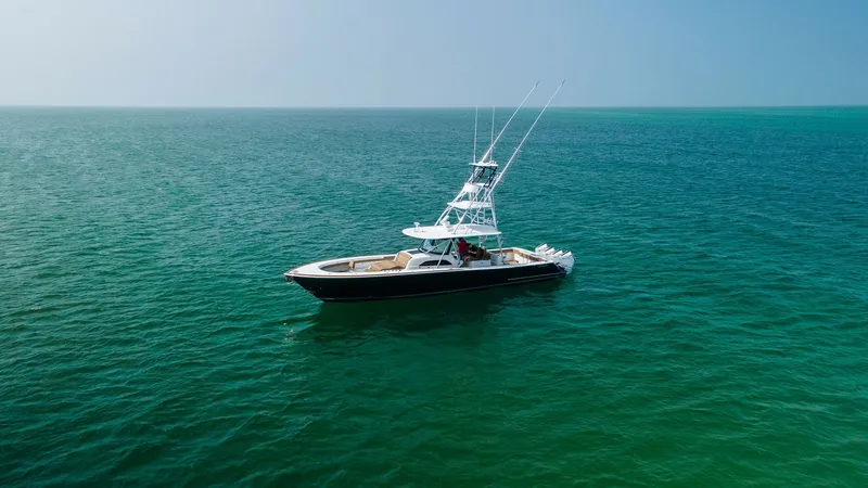 Slide: The Image of Aerial View of V-46 Sportfish The Valhalla Boatworks V-46, model year 2022, elegantly cruises through calm waters, showcasing its sleek design and powerful presence. The vessel features a spacious deck with ample seating and a robust tower equipped for sportfishing. Its deep blue hull - 6845084