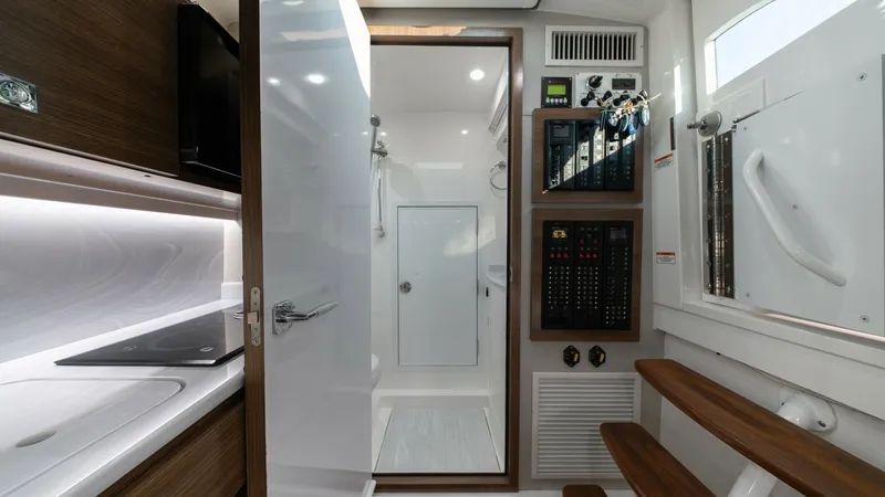 Slide: The Image of Interior Galley and Control Panel View This image showcases the sleek interior galley of the MarMar V-46 by Valhalla Boatworks. The space features modern wood finishes and a streamlined countertop with an integrated stovetop. Adjacent to the galley, a well-organized control panel is visible, h - 7162313