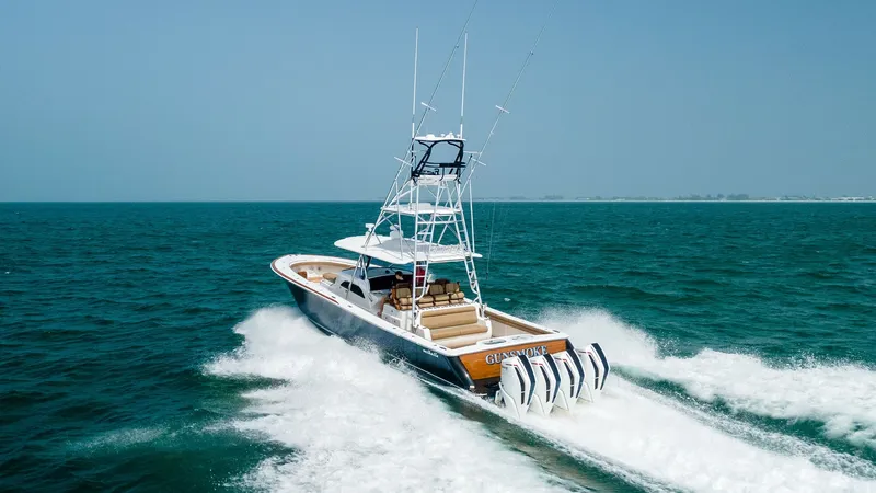 Slide: The Image of Aerial View of V-46 Aft Deck This dynamic image captures the aft deck of the Valhalla Boatworks V-46, showcasing its powerful quad outboard engines cutting through the turquoise waters. The spacious deck features elegant teak finishes and plush seating, perfect for both relaxation an - 6845096