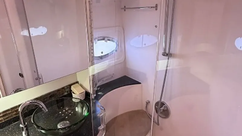 Slide: The Image of Elegant Ensuite Bathroom This luxurious ensuite bathroom features a sleek glass vessel sink and a modern faucet, set against a glossy black countertop. The curved shower area is fitted with high-quality fixtures and a convenient bench seat. Natural light filters through the porth - 6857436