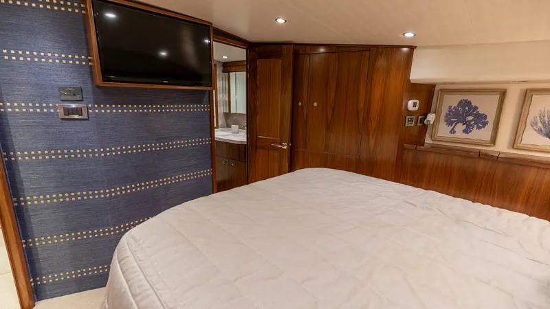 Slide: The Image of Master Stateroom with Ensuite View The master stateroom of the 2022 Viking 68 Convertible exudes luxury with its richly finished wood paneling and soft ambient lighting. A plush, expansive bed invites relaxation, while the integrated flat-screen TV ensures entertainment. The ensuite bathro - 7463809