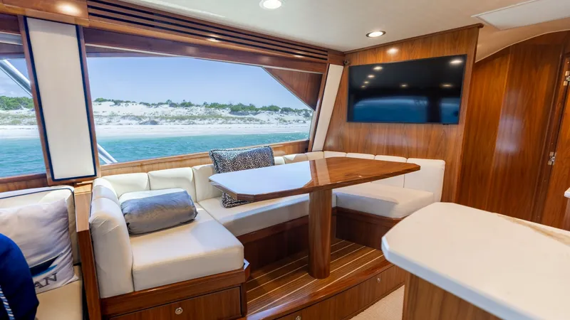 Slide: The Image of Salon with Dining and Panoramic View The salon of the 2022 Viking 68 Convertible showcases a spacious dining area with elegant wood finishes and plush seating. Large windows offer a breathtaking panoramic view of the surrounding seascape, enhancing the luxurious ambiance. The built-in TV pro - 7463805