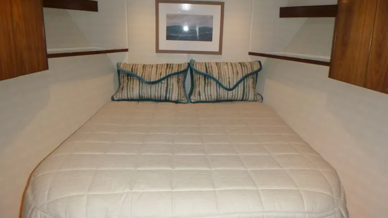 Slide: The Image of Forward Guest Stateroom This inviting forward guest stateroom on the 2022 Viking 68 Convertible showcases a plush double berth, accented with elegant striped pillows. The warm wood cabinetry and soft lighting create a cozy ambiance, while ample storage is seamlessly integrated i - 6862343