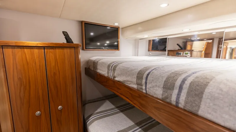 Slide: The Image of CrewStateroom with Bunk Beds This cozy crew stateroom on the Viking 68 Convertible features well-crafted bunk beds with elegant wood finishes. The soft, striped bedding complements the warm wood tones, creating a welcoming atmosphere. A flat-screen TV and ample storage enhance comfor - 7463821