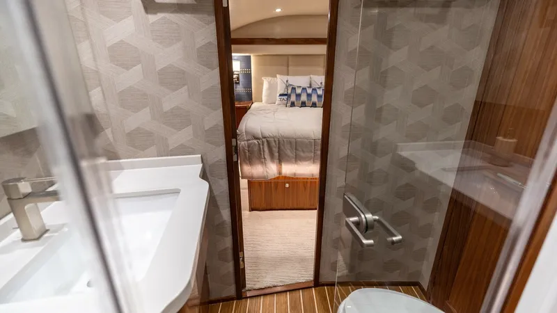 Slide: The Image of Ensuite Bathroom and Stateroom View This image captures the elegant ensuite bathroom aboard the Viking 68 Convertible, featuring modern fixtures and a sleek vanity. The warm wood flooring and geometric wall patterns enhance the sophisticated ambiance. Beyond the bathroom, the plush stateroo - 7463810