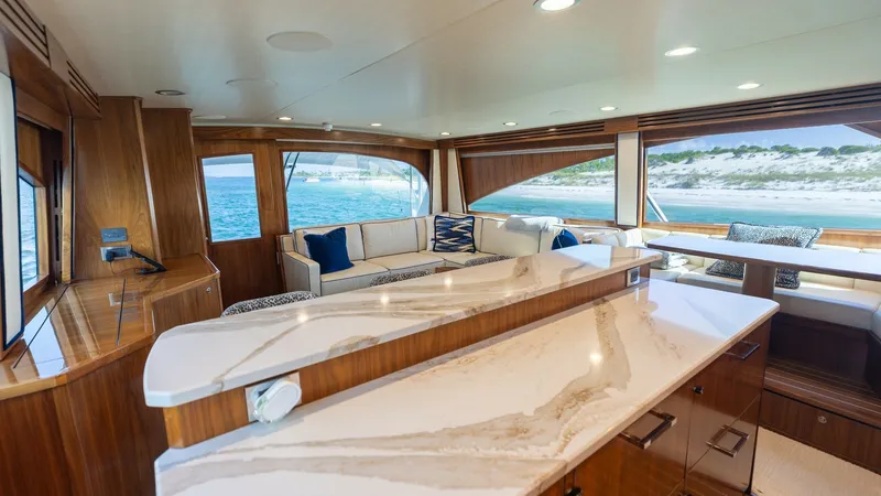 Slide: The Image of Spacious Salon with Ocean Views The salon of the 2022 Viking 68 Convertible offers an inviting and luxurious atmosphere, featuring a beautifully crafted marble countertop and rich wood finishes. Expansive windows provide stunning ocean views, flooding the space with natural light. The e - 7463804