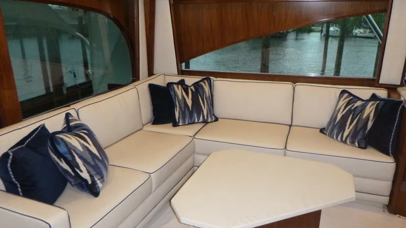 Slide: The Image of Luxurious Salon Seating Area The salon of the 2022 Viking 68 Convertible offers an inviting and spacious seating area with plush cream upholstery accented by navy and patterned throw pillows. Rich wooden finishes frame large windows, providing ample natural light and picturesque view - 6862328
