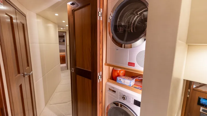 Slide: The Image of Hallway with Laundry Appliances This image showcases the hallway of the 2022 Viking 68 Convertible, featuring a convenient built-in laundry area. The neatly integrated washer and dryer are enclosed behind elegant wooden cabinetry, blending functionality with style. Soft ambient lighting - 7463822