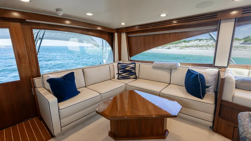 Slide: The Image of Elegant Salon with Ocean Views The salon of the 2022 Viking 68 Convertible offers a luxurious seating area with plush, cream-colored upholstery accented by navy blue cushions. The space is beautifully illuminated by ample natural light streaming through large windows that provide stunn - 7463799