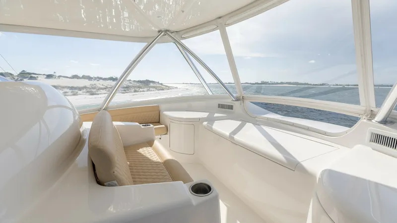 Slide: The Image of Flybridge Helm Seating Area The flybridge of the 2022 Viking 68 Convertible offers a luxurious seating area with panoramic views. The plush, tan upholstery complements the sleek, white surfaces, enhancing the elegant design. Large windows provide ample natural light, creating an inv - 7463825